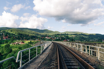 Fototapeta na wymiar Railway track on the bridge on the background of a beautiful mountain landscape. Suburban railway on the background of the village and mountains. Vorokhta. Ukraine, Carpathians