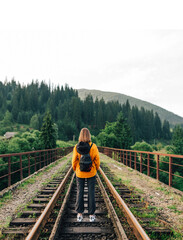View from the back, a woman stands on a railway track in Vorokhta, Carpathians, Ukraine and looks at a beautiful mountain landscape. Vertical.
