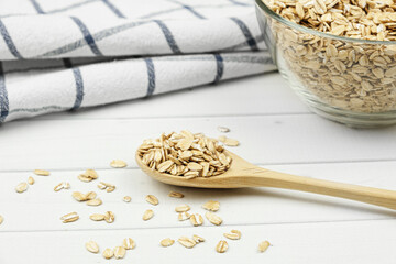 Wooden spoon with oatmeal, a glass bowl of oatmeal and a tea towel on light wooden boards. Healthy food concept, breakfast with cereals. Selective focus on a spoon, blurred background.