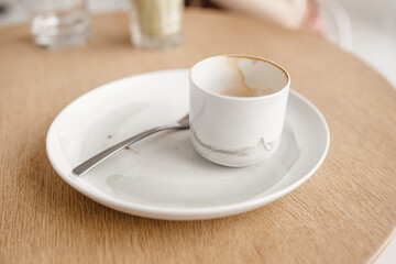 Used empty cup of coffee with a white plate and fork on a wooden table in a cafe