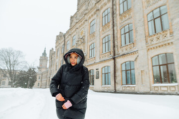 Fototapeta na wymiar The lady fastens her coat during a walk in the winter season in the snowfall on the street against the backdrop of snowy views and historic architecture.