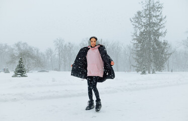 Full length portrait woman in warm winter clothes in the snow stands on the street and enjoys the...