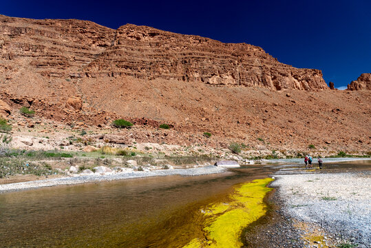 Images of Morocco. A view of the bottom of the Ziz river gorges, with the contrast between the red cliff, the white gravel bottom and the yellow green algae.