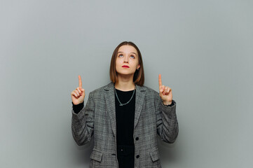 Beautiful woman in office worker jacket looking up and pointing fingers at copy spacee