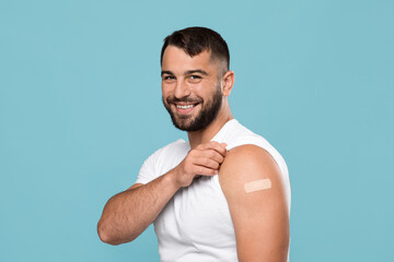 Smiling adult attractive caucasian guy show shoulder with band aid after vaccination - obrazy, fototapety, plakaty