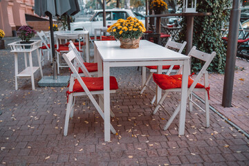 Wooden table with transparent glass vase with yellow flowers. Street urban cafe during lockdown, coronavirus quarantine