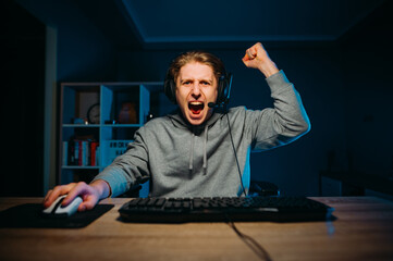 Joyful gamer rejoices in winning the game sitting at the computer is given to the screen and...