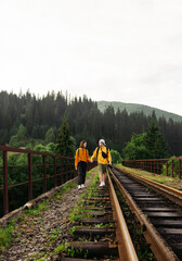 Couple in love with tourists standing on the tracks of a railway bridge in the mountains holding hands against the backdrop of an unreal mountain landscape. Vertical