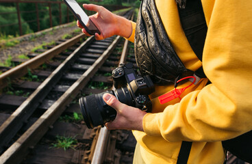 Male tourist holds a camera in his hands and uses a smartphone on the background of the railway track, close-up photo.