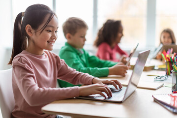 Diverse Children Learning Using Laptop In Modern Classroom At School