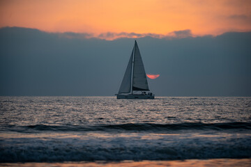 Sailing in the sunrise time with sailboat. Sunrise over the sea and beautiful cloudscape. Colorful ocean beach sunset.