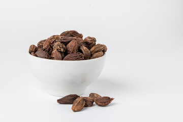 Fragrant oriental spices black cardamom pods with seeds in a small white ceramic boul with copy space
