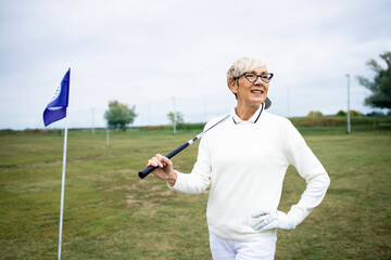 Portrait of senior gray haired woman playing golf on golf course.