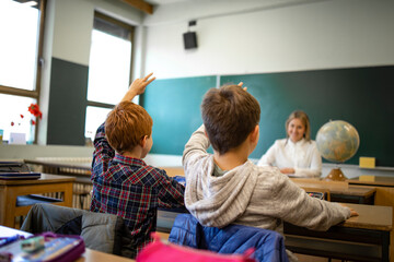 Obraz premium Schoolchildren at classroom with raised hands answering teacher's question.