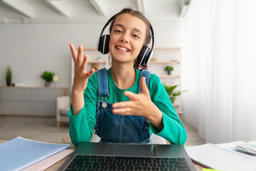Smiling girl in headset using laptop, talking during videochat