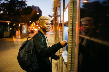 Young latin american male with a blue credit card  on a bank cashier, at dusk