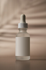 a bottle of serum with a pipette on a beige sand background 