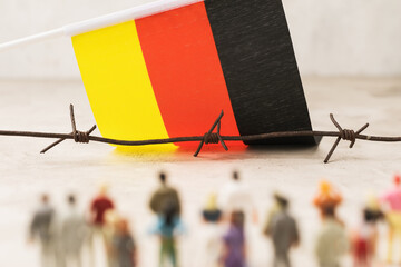 Barbed wire, flag of Germany and plastic toy men out of focus, concept of illegal border crossing...