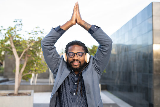Afro man in suit and with glasses does yoga outdoors while listening to music with headphones
