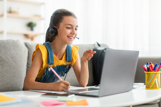 Smiling girl in headset using laptop, talking during videocall - Powered by Adobe