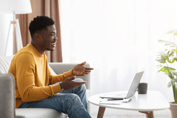 Cheerful black guy having video call with girlfriend, using laptop