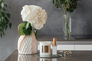 Stylish tender composition with candles, wick trimmer, lollion and flowers on table against gray...