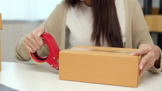 Close up business woman hand packing product sealing cardboard with duct tape. Startup Small business owner entrepreneur packing product in the box
