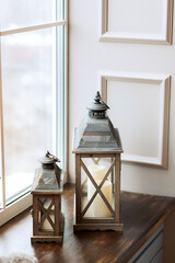 Two antique lanterns with candles stand by the window. Light background. Christmas home decoration.