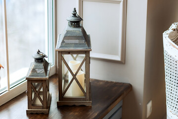Two antique lanterns with candles stand by the window. Light background. Christmas home decoration.