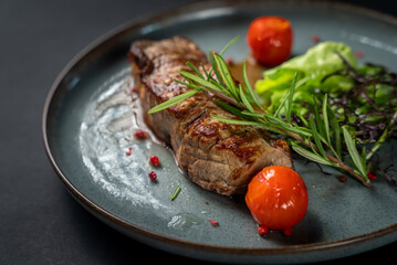Roasted steak with spices and cherry tomatoes. Close up shot. Juicy steak with green vegetables on black background. Tasty dinner with friends in restaurant. Copy space. 
