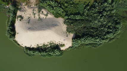 Top view of an abandoned sandy beach with vegetation around and a green lake