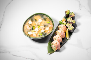 Sushi set and miso soup on white background. Maki roll for lunch offer or business lunch. Japanese traditional healthy food. KETO diet, low-carb sushi without rice. Restaurant menu. Copy space