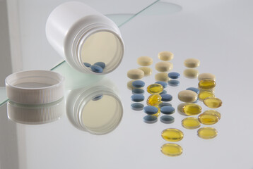 blue and yellow coated tablets and yellow soft capsules in front of opened white plastic bottle
