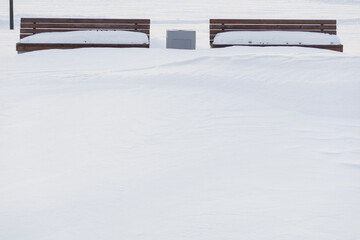 Deep snow covered space in front of two benches in a winter park