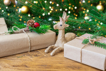 Christmas eco-friendly gifts wrapped in wrapping paper on a wooden table with fir branches and a garland. A papier-mache deer figurine. Selective focus. Close-up, copy space,concept Christmas
