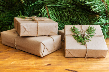 Christmas eco-friendly gifts wrapped in wrapping paper, decorated with twigs of greenery, lie on wooden table with pine branches. Close-up, copy space. The concept of celebrating Christmas, New Year