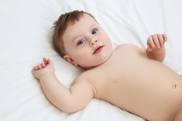 A boy in diapers on a bed in a snow-white bedroom