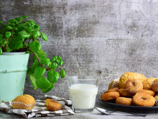 Glass of milk, next to it muffins and doughnuts on a plate, decorative contour, base and bottom of stone.