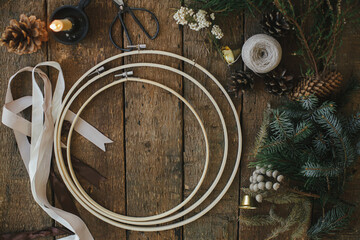 Making modern christmas wreath, rustic flat lay. Fir branches, brunia herb, ribbons, round wooden hoops, scissors, thread on rustic table. Atmospheric image. Winter holidays preparation