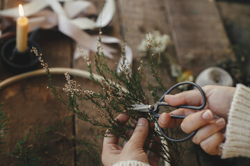 Making stylish minimalist christmas wreath. Hands cutting branch with scissors for modern boho...