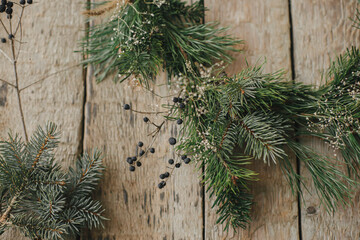 Modern christmas wreath with spruce branches, herbs, berries on rustic wood. Merry Christmas! Stylish boho xmas wreath details close up. Moody image, winter holiday preparation
