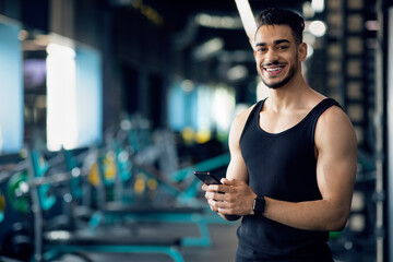 Portrait Of Smiling Handsome Arab Guy Using Smartphone While Training In Gym