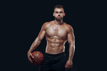 Fototapeta premium Portrait of a very muscular naked man playing basketball isolated on black background