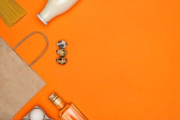 Paper eco bag, glass bottle of milk, white and quail eggs, spaghetti, olive oil on orange background. Healthy food, delivery, donation concept. Food stock for quarantine. Top view, flatly, copyspace