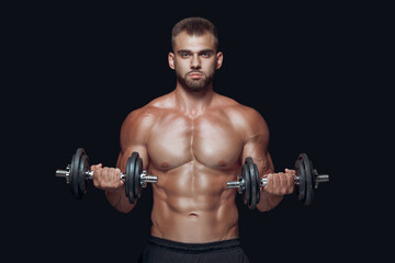 Front view of strong athletic man lifting dumbbells looking at camera isolated over black background