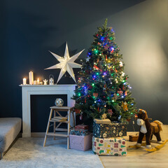 Home decoration before Christmas. Decorated Christmas tree with garland lights, rocking horse, gifts wrapped in elegant paper, artificial fireplace with a large white paper star and candles.