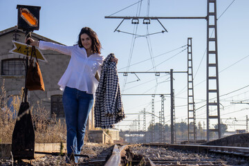 Young female traveler waiting for the railroad leaning and keeping balance on the railroad switch on the railroad track a beautiful background. Concept train, via, station, wagon.