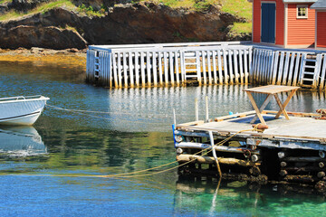 A small boat moored to pier, fishing sheds and another pier in the background.