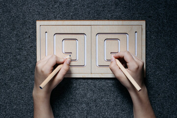 Child hands drawing lines in two-sided wooden stencil labyrinth