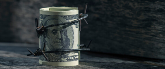 Economic warfare, sanctions and embargo busting concept. Close up US Dollar money wrapped in barbed...